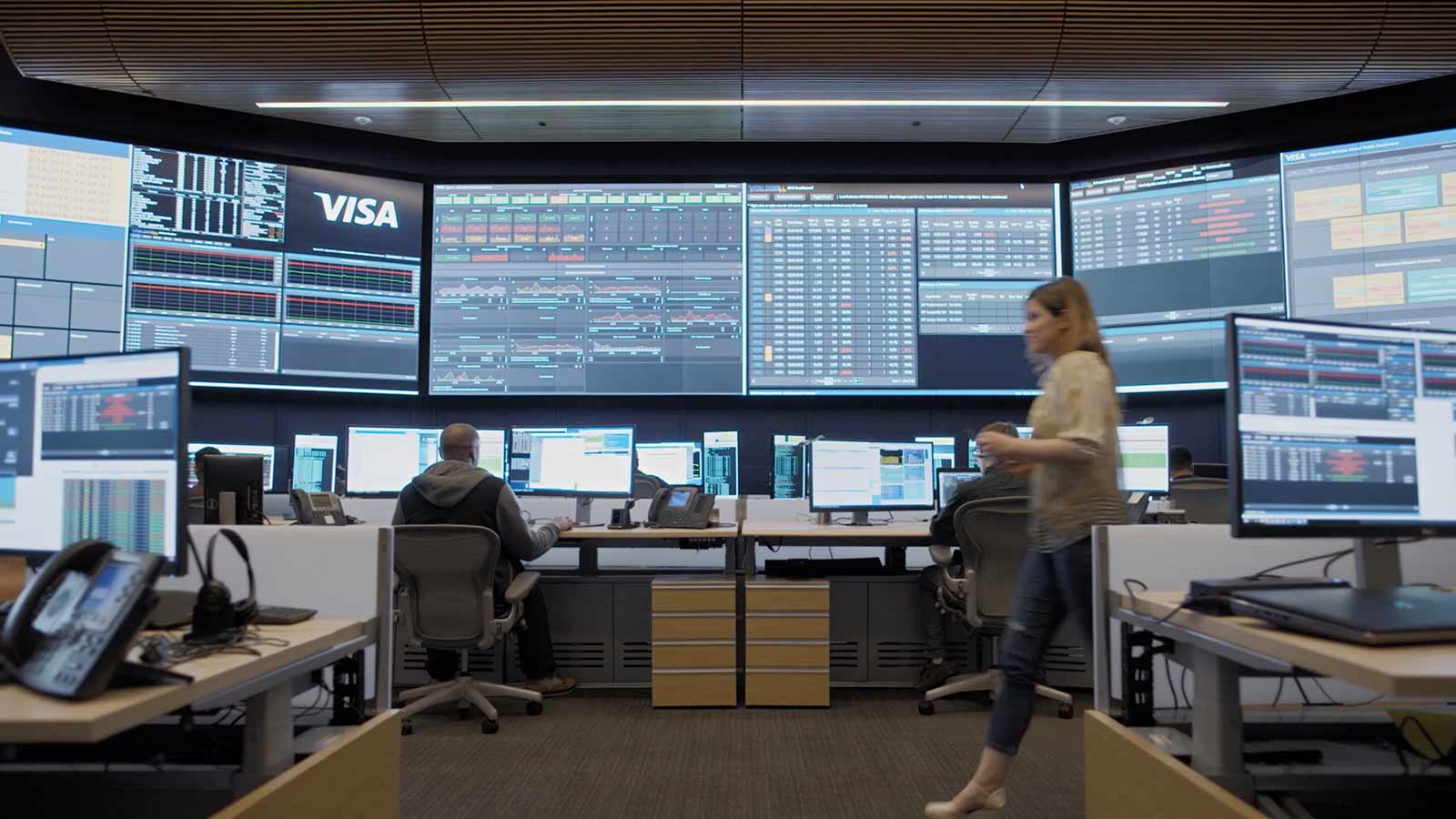 A man working in a security intelligence office and a woman walking by.