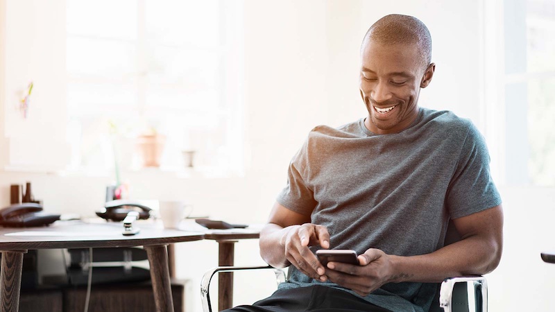 642394501 Man using his smartphone while sitting on a chair near a desk.