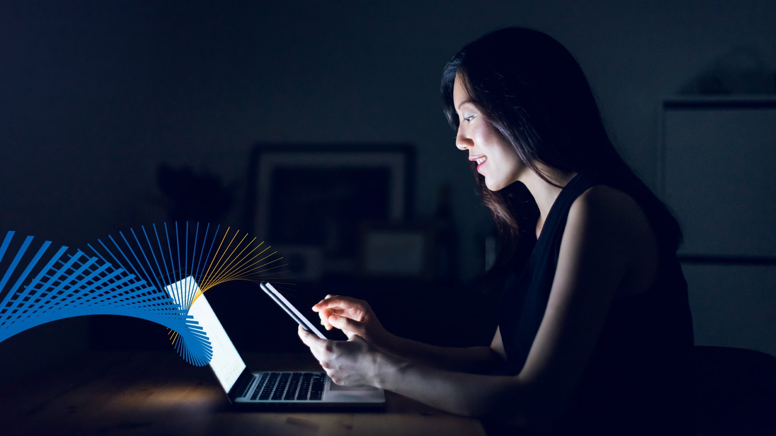 Women sitting in front of laptop, but looking at mobile phone.