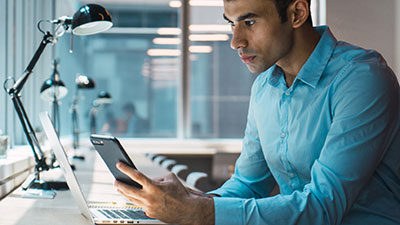 Young man using phone while working on laptop