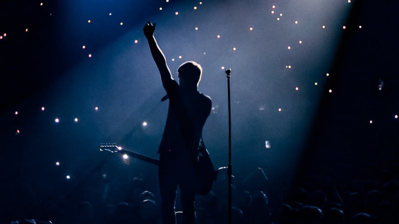 A person holding a guitar and standing on a stage with a microphone